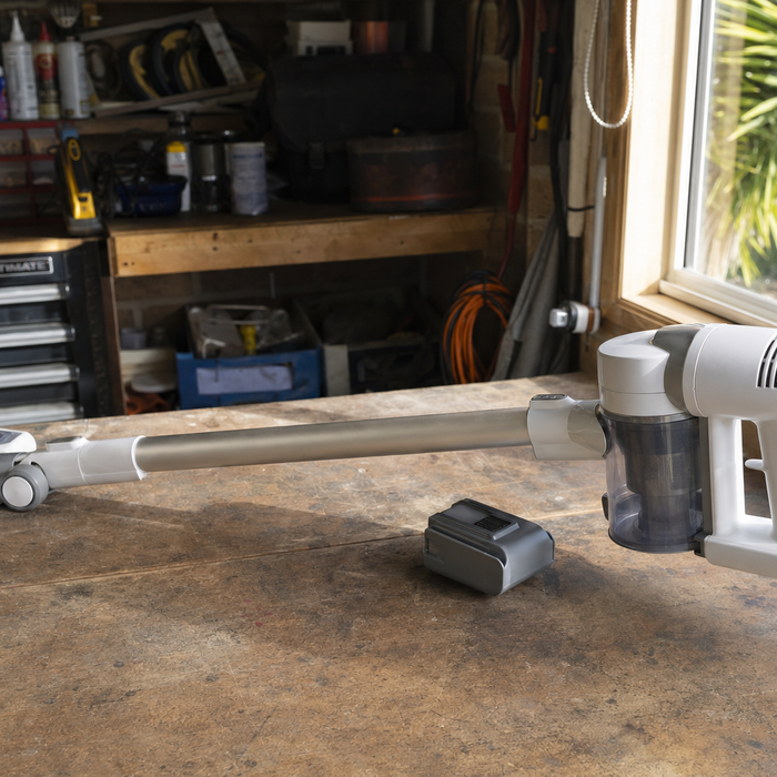 Cordless stick vacuum with detached battery pack lying on a workbench in a home garage
